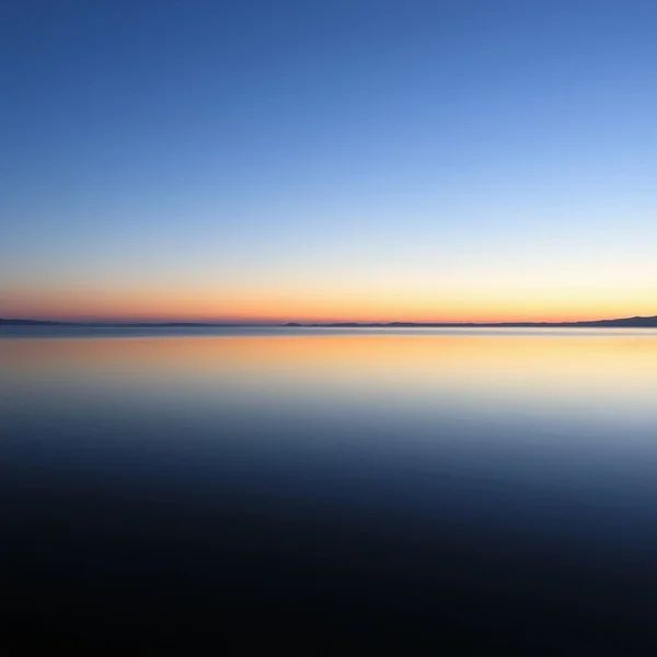 Synonyms for Serene: A peaceful, calm lake at dusk reflecting the sky